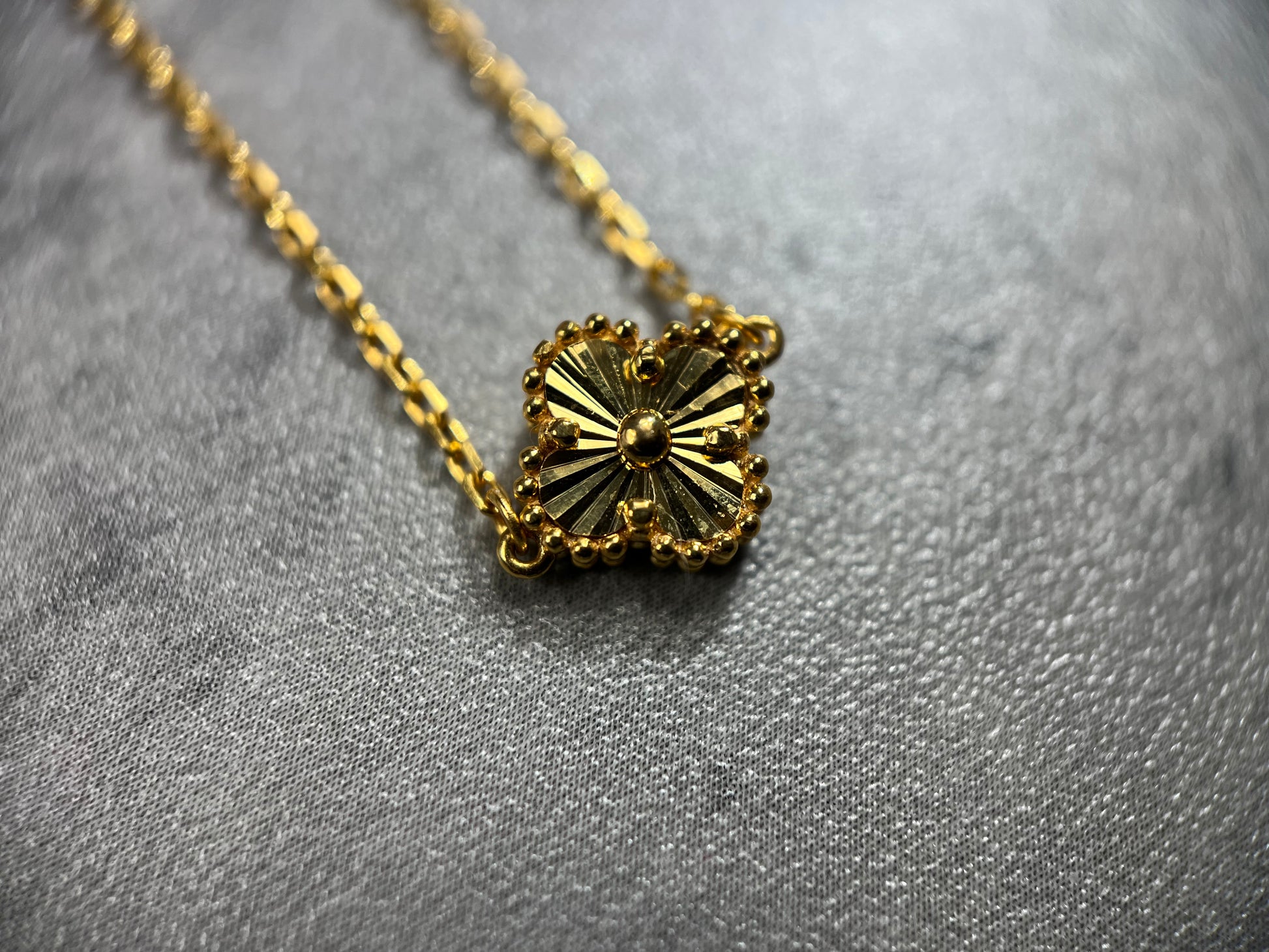 Close up picture of the clover flower. Our exquisite 22ct Yellow Gold Hallmarked Clover Necklace—a symbol of luck and beauty. This necklace features 5 delicately crafted clover designs with flower motifs and a secure Lobster Clasp. With a highly polished finish, it radiates elegance. Length: 18" (45.7cm). Also available in 3, 5, & 10 Clovers in different lengths. Elevate your style with this timeless and versatile gold necklace today.