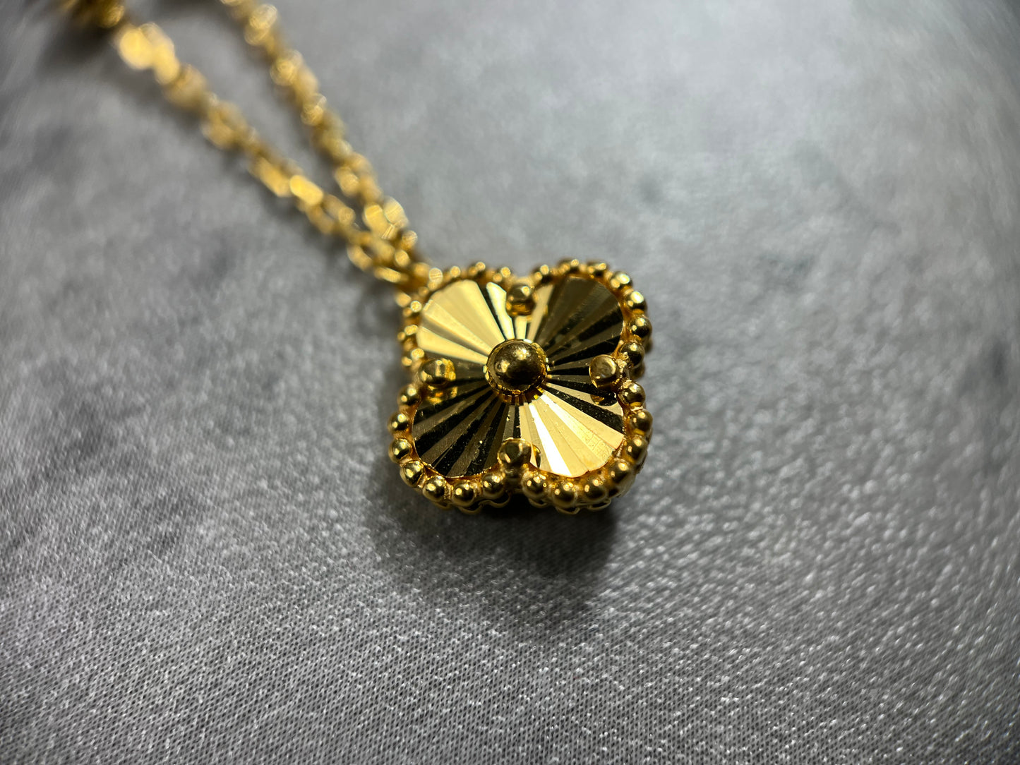 A close-up picture of our elegant 22ct Yellow Gold Hallmarked Clover Necklace—an exquisite and popular piece. This necklace features 3 charming clover designs, each adorned with a flower motif and a secure Lobster Clasp. With a highly polished finish, it radiates timeless allure. Length: 18" (45.7cm). Also available in 3, 5, & 10 Clovers in different lengths. Elevate your style with this versatile and finely crafted gold necklace today.