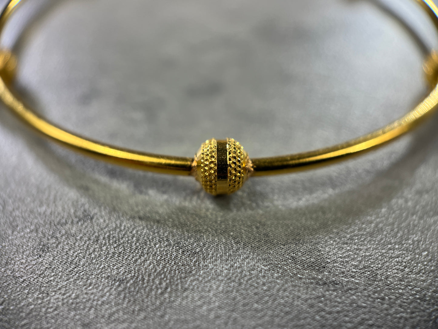 Close up picture of our exquisite 22ct Yellow Gold Hallmarked Single Ball Bangle—a stunning blend of elegance and craftsmanship. Adorned with six delicately hand-carved balls, each featuring intricate indented spots, this bangle exudes sophistication. With a highly polished finish, it catches the light beautifully. Each bangle comes with premium gift packaging, making it a thoughtful and cherished present. Elevate your style with this finely crafted gold bangle—a true symbol of timeless allure.