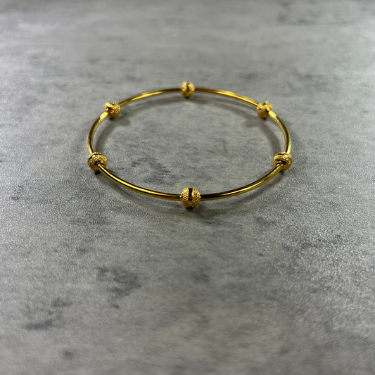 Our exquisite 22ct Yellow Gold Hallmarked Single Ball Bangle—a stunning blend of elegance and craftsmanship. Adorned with six delicately hand-carved balls, each featuring intricate indented spots, this bangle exudes sophistication. With a highly polished finish, it catches the light beautifully. Each bangle comes with premium gift packaging, making it a thoughtful and cherished present. Elevate your style with this finely crafted gold bangle—a true symbol of timeless allure.