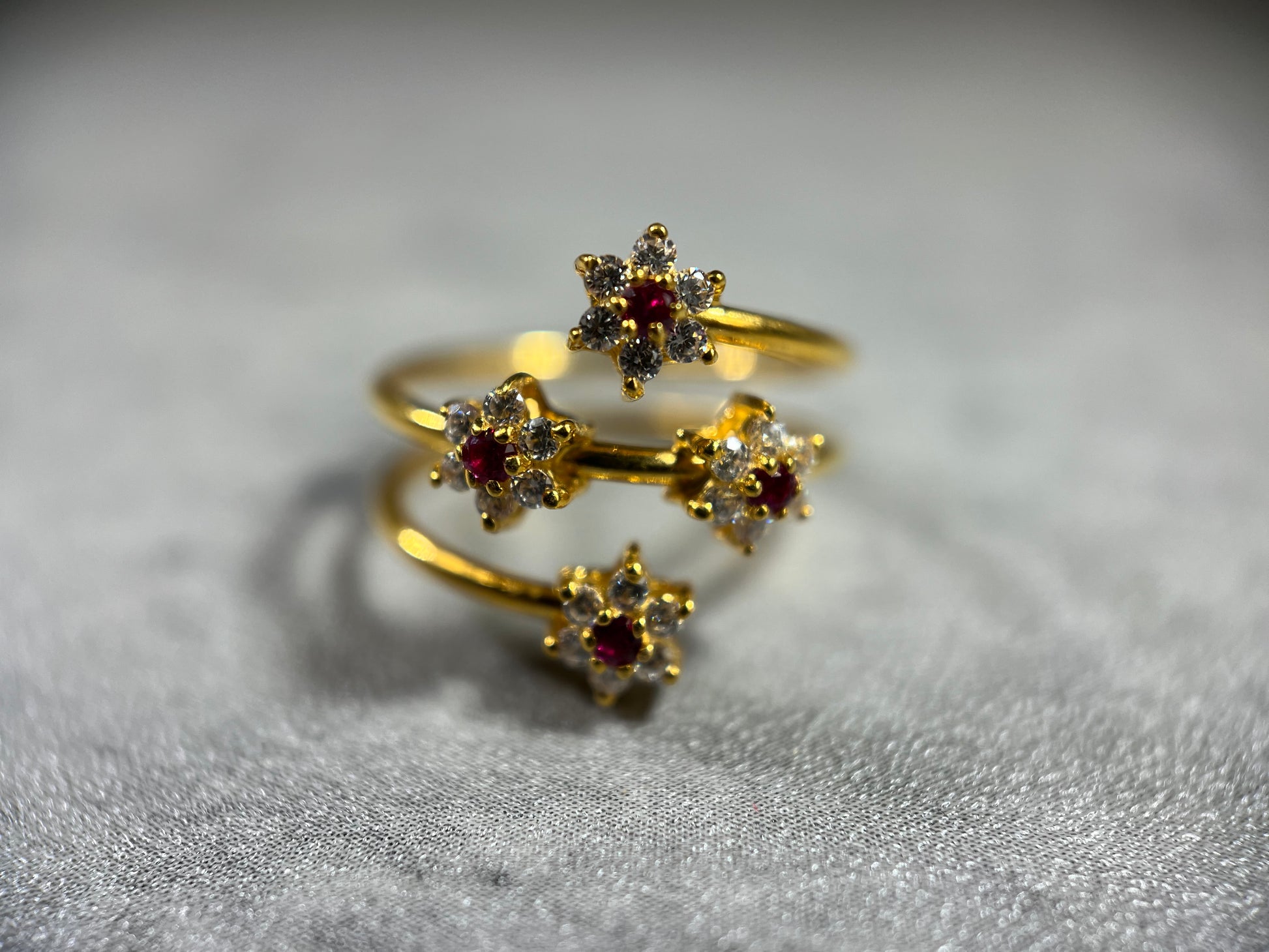 This elegant Gold Triple Wire Ring, featuring a stunning flower design with four radiant gemstones in a flower design (centre stone is red). Crafted from 22K gold, this masterpiece exudes sophistication and grace. The intertwined bands ensure a comfortable fit for any occasion. Elevate your style with the timeless beauty of nature and the brilliance of gemstones in this unique and exquisite ring!