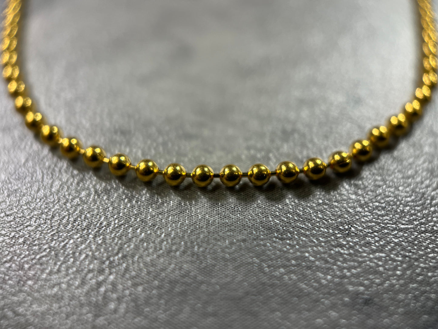 Close up picture of the necklace. Our 22ct Yellow Gold Hallmarked Small Ball Chain—a symbol of simplicity and elegance. With connecting balls along the chain and a highly polished finish, this piece radiates sophistication. Length: 18" (45.7cm). Available in various lengths—just get in touch. Each chain comes with packaging, making it a perfect gift choice. Elevate your style with this beautifully crafted gold chain today.