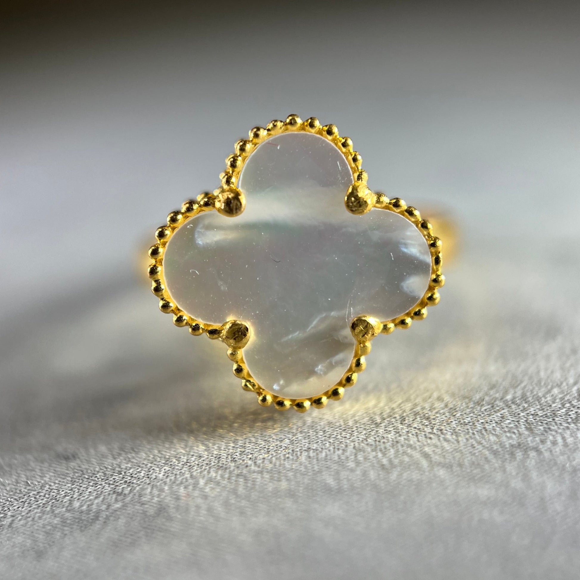 A close up picture of our elegant 22ct Yellow Gold Hallmarked Mother of Pearl Clover Ring—a popular and versatile piece. With a simple flower design and a highly polished finish, this ring exudes sophistication. The mother of pearl stone at the center of the clover flower adds a touch of elegance. It can be worn alone for a subtle look or stacked with other rings for a stylish statement. Elevate your style with this beautifully crafted gold ring—a perfect addition to your jewelry collection.