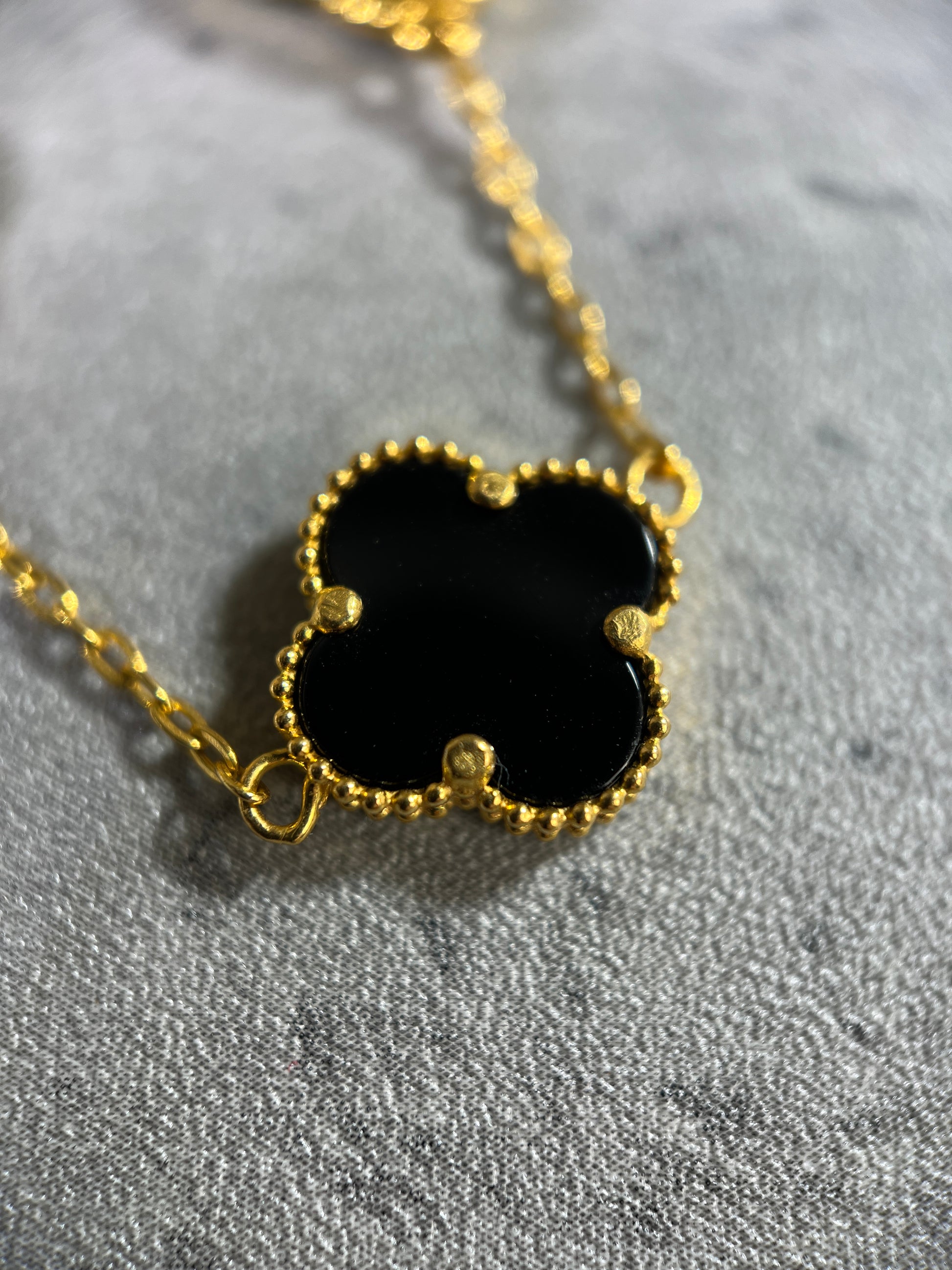 Close up picture of the onyx clover. A 8 clover onyx necklace in 22ct yellow gold hallmarked. The design of the onyx is of a 4 petal flower, and the clasp of the bracelet is a lobster clasp. Length of necklace is 18 inches. The item is ready for purchase, and is perfect as a treat for oneself, a gift for a family or friend! This necklace is a statement piece, can be worn on its own or stacked alongside other necklaces. 